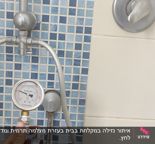 מד לחץ מים מוחזק ביד ליד צינור במקלחת